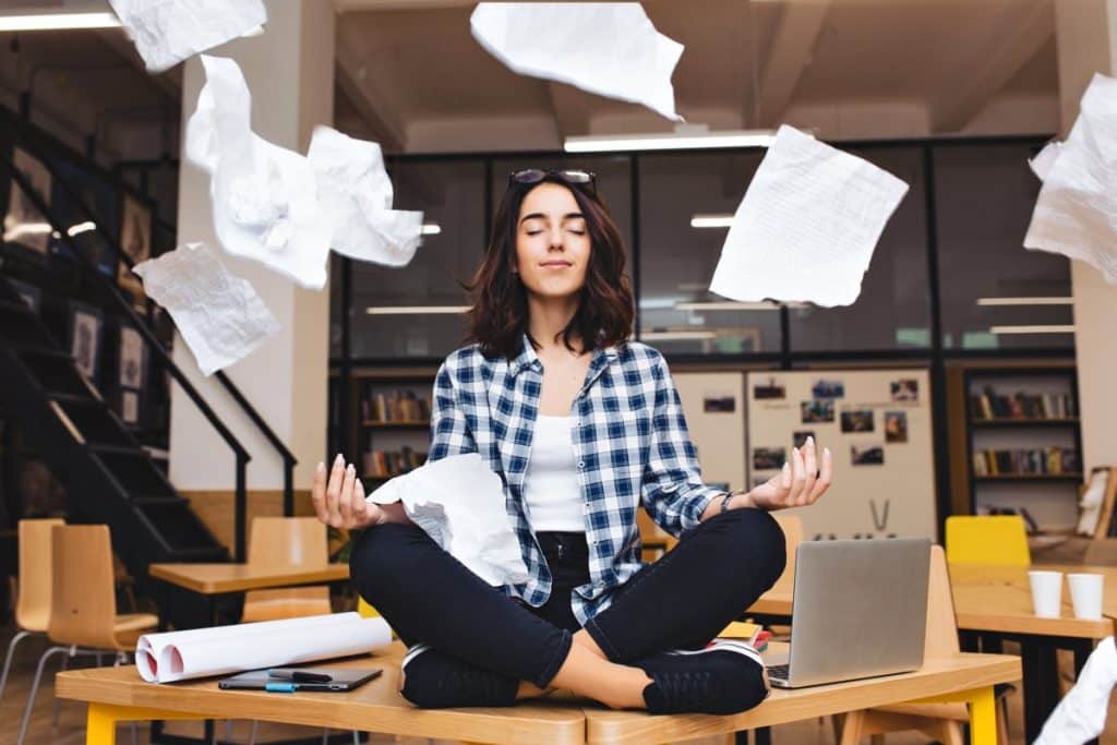 Mujer tratando de meditar sentada sobre una mesa de estudio para mejorar la gestión de las emociones